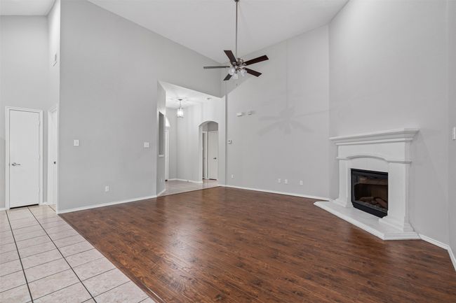 Unfurnished living room with a ceiling fan, high vaulted ceiling, a fireplace with raised hearth, arched walkways, and wood finished floors | Image 18