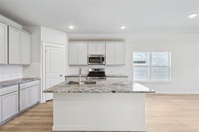 Kitchen featuring backsplash, light wood-type flooring, light stone counters, stainless steel appliances, and a kitchen island with sink | Image 2