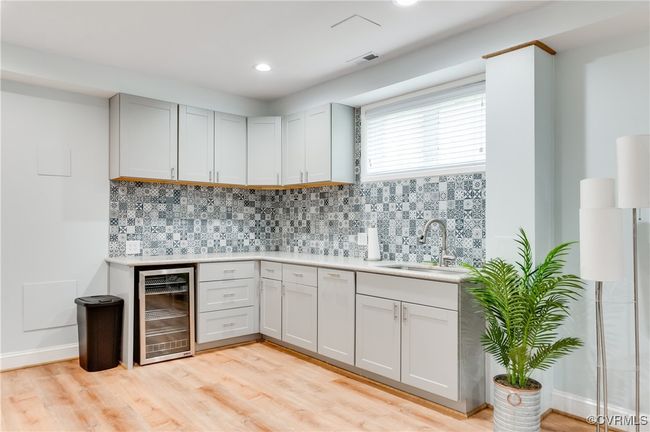 Kitchen with light countertops, a sink, wine cooler, and tasteful backsplash | Image 24