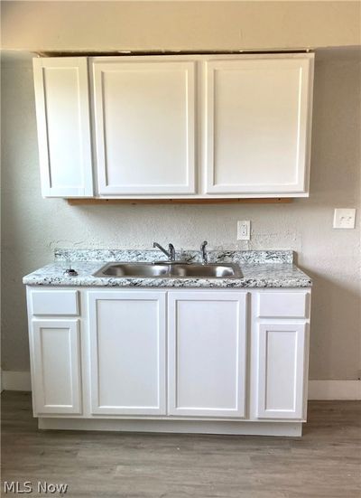 Kitchen with white cabinets, light hardwood / wood-style flooring, light stone counters, and sink | Image 3