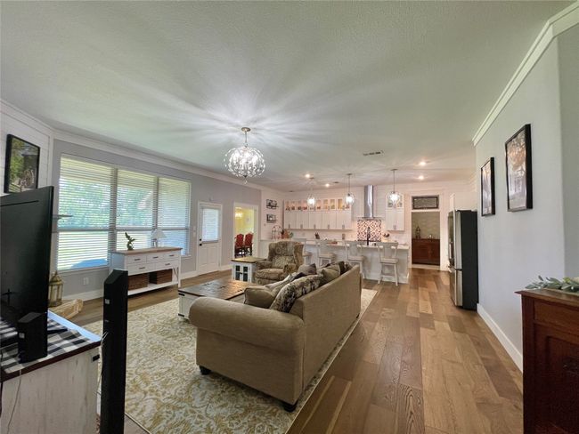 Living room with ornamental molding, a chandelier, light wood-type flooring, baseboards, and recessed lighting | Image 10