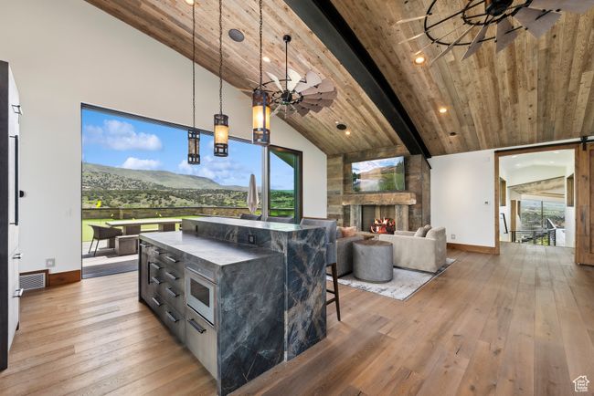 Living area featuring baseboards, light wood finished floors, a stone fireplace, a ceiling fan, and high vaulted ceiling | Image 114