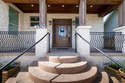 Charming entrance featuring a stone facade, elegant wooden door, and decorative iron railing, complemented by a welcoming semi-circular staircase. | Image 2