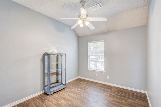 Empty room with ceiling fan, wood finished floors, a textured ceiling, vaulted ceiling, and baseboards | Image 7