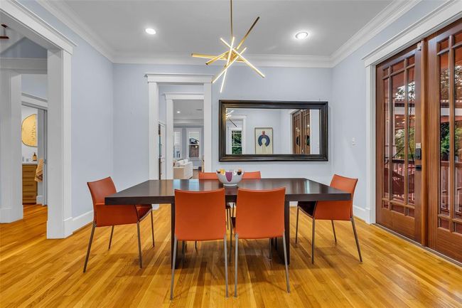 The elegant formal dining room features a modern light fixture, elegant hardwood floors, and opens to the home-office as well as the butler's pantry. Large wooden doors lead to the wraparound porch, providing ample natural light, and a large mirror adds depth to the room. | Image 10