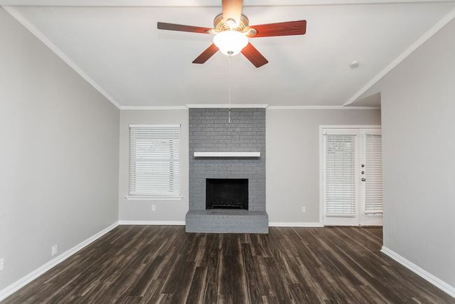 Unfurnished living room featuring dark wood-type flooring, a brick fireplace, ceiling fan, and ornamental molding | Image 4