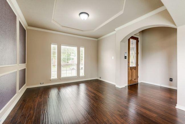 Empty room with arched walkways, dark wood finished floors, and a raised ceiling | Image 5