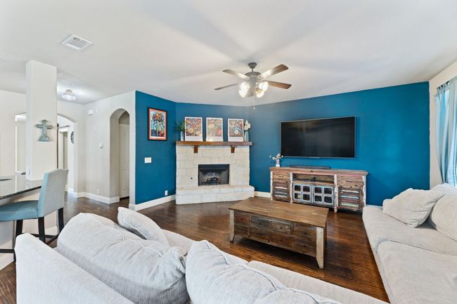 Living area with visible vents, baseboards, ceiling fan, a stone fireplace, and dark wood-style floors | Image 10