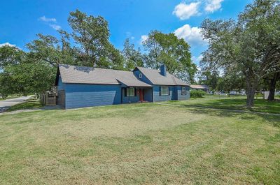 Nestled on a spacious .43 acre corner lot, this charming farmhouse-style home in Hempstead showcases a fresh exterior paint in a soothing blue tone. The house's welcoming presence is accentuated by the lush green lawn and mature trees, providing a serene setting just moments away from Hempstead City Park and local schools. | Image 1