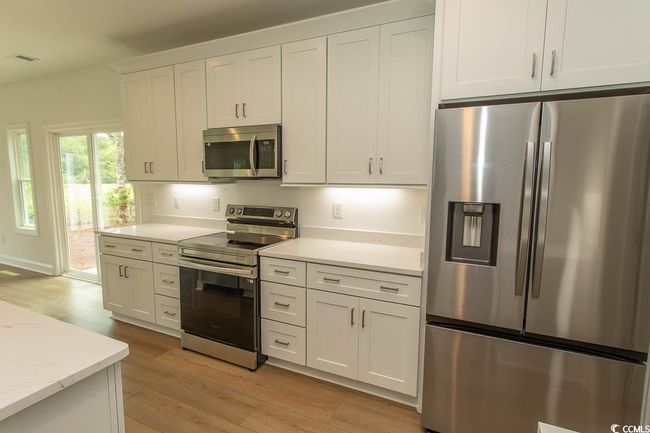 Kitchen with stainless steel appliances, light wood finished floors, white cabinetry, and light stone countertops | Image 6