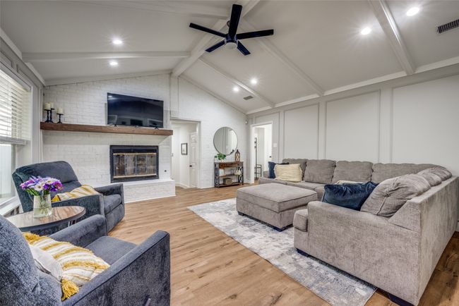 Living room with wood finished floors, a brick fireplace, ceiling fan, and a decorative wall | Image 4