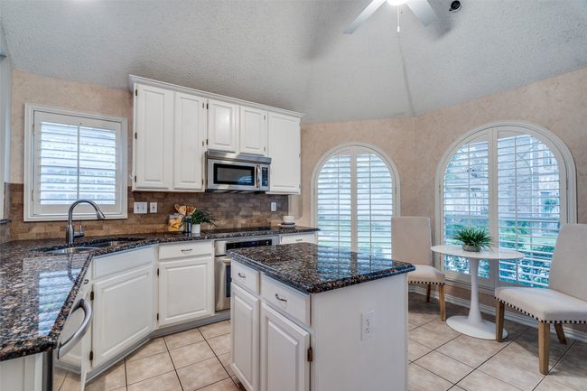 Kitchen featuring stainless steel appliances, lofted ceiling, light tile patterned floors, dark stone countertops, and white cabinetry | Image 7