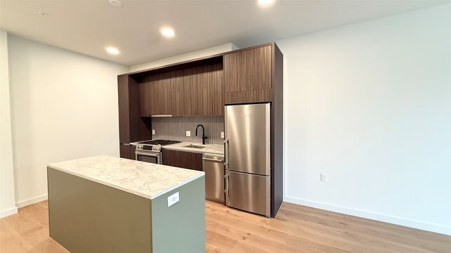 Kitchen with appliances with stainless steel finishes, light countertops, backsplash, a center island, and light wood-style flooring | Image 14