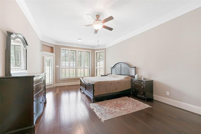 Spacious primary suite featuring rich wood flooring, crown molding, and large windows with plantation shutters for natural light and privacy. | Image 24