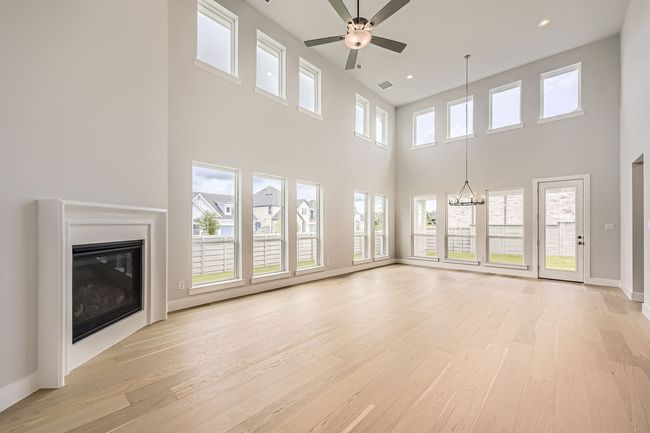 Unfurnished living room featuring a glass covered fireplace, light wood-type flooring, a chandelier, a ceiling fan, and a towering ceiling | Image 7