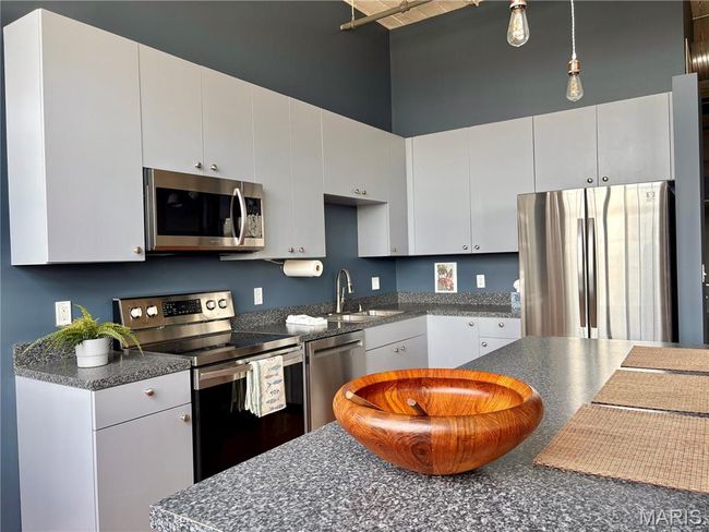 Kitchen with stainless steel appliances, dark countertops, white cabinets, a towering ceiling, and hanging light fixtures | Image 11