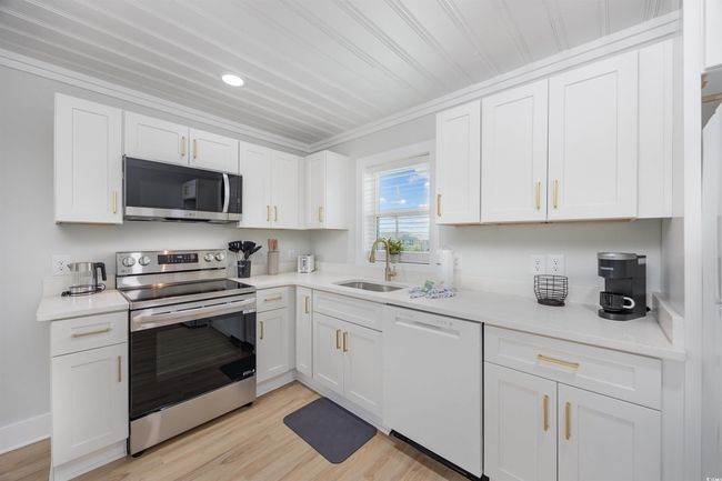 Kitchen featuring appliances with stainless steel finishes, a sink, white cabinets, light countertops, and ornamental molding | Image 25