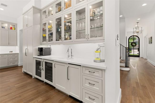 Wet bar w/ sink, wine fridge, ice maker w/ wood paneled front, glass shelving & glass front cabinets w/ lighting, under cabinet lighting. | Image 25