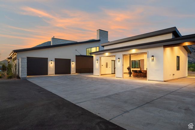 Back of house at dusk featuring concrete driveway, an attached garage, stucco siding, and a chimney | Image 70