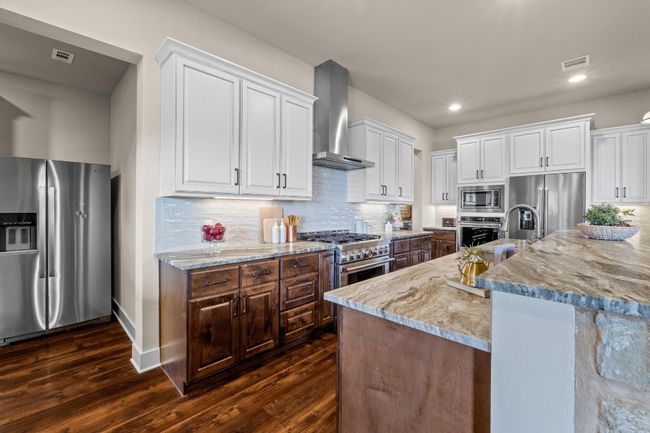 Kitchen featuring white cabinets, high end appliances, dark wood finished floors, wall chimney exhaust hood, and visible vents | Image 11