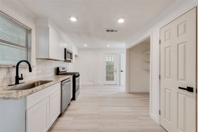 Kitchen with a sink, decorative backsplash, white cabinetry, appliances with stainless steel finishes, and visible vents | Image 11