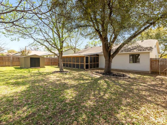 Back of property featuring an outbuilding, a sunroom, a fenced backyard, a yard, and a storage shed | Image 24