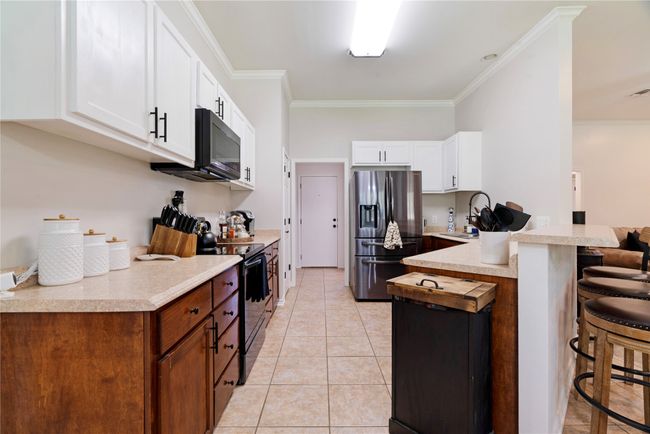 Kitchen featuring a sink, black appliances, light tile patterned flooring, a breakfast bar, and a peninsula | Image 8