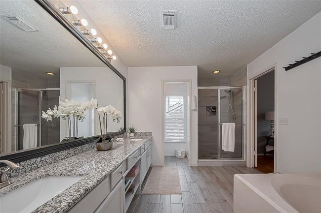 The primary bathroom offers a spacious granite countertop with an extended mirror, providing plenty of room for daily routines. Enjoy the comfort of a relaxing garden tub and the convenience of a separate walk-in shower, creating a perfect blend of luxury and functionality. | Image 18