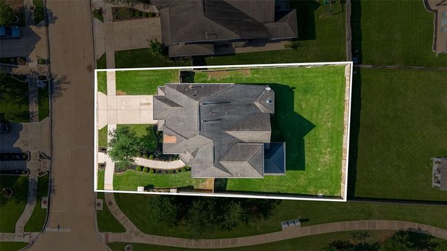 This aerial photo shows a well-maintained home with a spacious yard, situated on a corner lot. The property features a large driveway, landscaped pathways, and is bordered by sidewalks. | Image 47