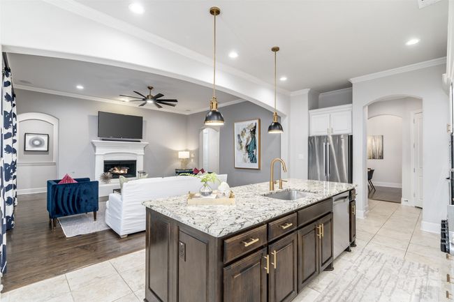 Kitchen walks through to dining area with a butler's station and the island features cabinet pulls, under mount sinnk with gold hardware and pendant lighting. | Image 12
