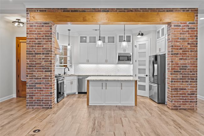 Kitchen featuring decorative backsplash, ornamental molding, stainless steel appliances, white cabinets, and a kitchen island | Image 7