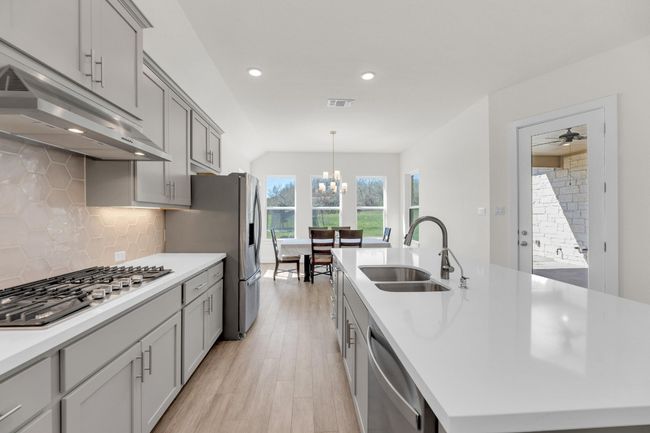 Kitchen with stainless steel appliances, light countertops, a sink, an island with sink, and under cabinet range hood | Image 13