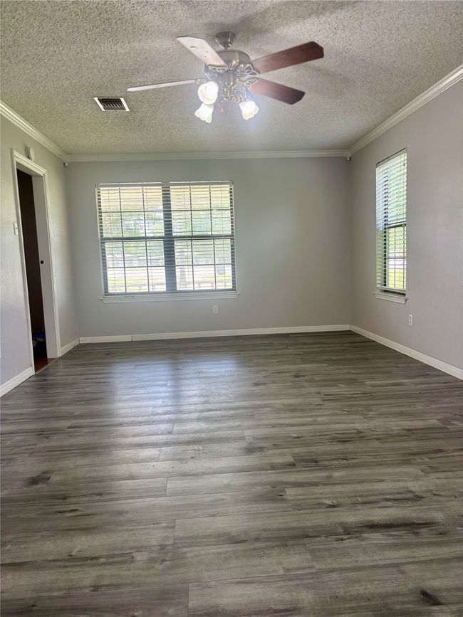 Empty room with crown molding, a textured ceiling, ceiling fan, and dark wood finished floors | Image 12