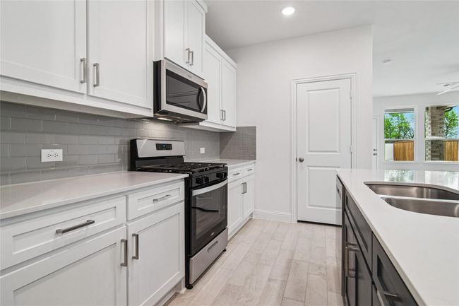 Kitchen featuring stainless steel appliances, white cabinetry, decorative backsplash, light stone countertops, and recessed lighting | Image 24