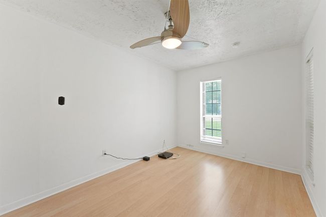 This room features a clean and minimalistic design with white walls, light wood flooring, and a ceiling fan. It has a window that allows natural light, creating a bright and airy feel. Perfect for a small bedroom or office space. | Image 6