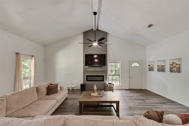 Living area with a large fireplace, high vaulted ceiling, beamed ceiling, wood finished floors, and ceiling fan | Image 5