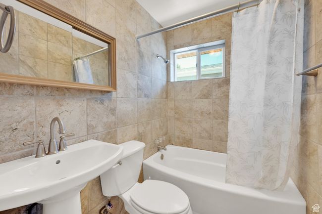 Bathroom with tile walls, a sink, shower / tub combo with curtain, and toilet | Image 12