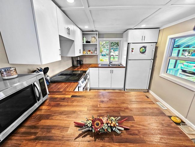 Kitchen featuring stainless steel microwave, freestanding refrigerator, open shelves, a sink, and range with electric stovetop | Image 7