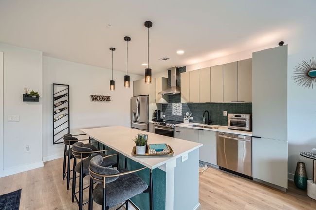 Kitchen with wall chimney range hood, appliances with stainless steel finishes, a breakfast bar, light countertops, and light wood-style floors | Image 7