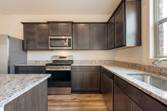 Kitchen featuring appliances with stainless steel finishes, light wood-type flooring, light stone countertops, and plenty of natural light | Image 4