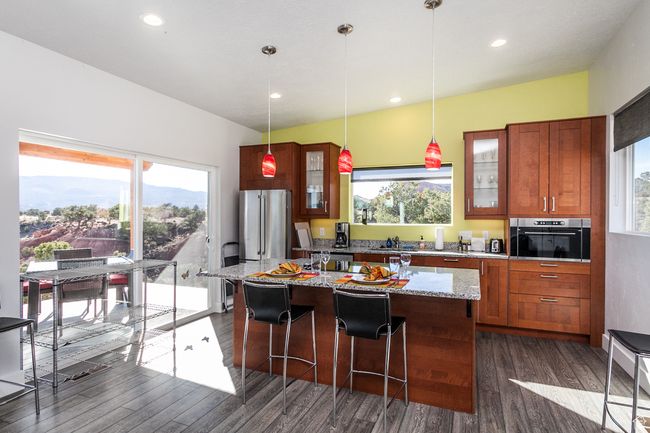 Kitchen with a breakfast bar, appliances with stainless steel finishes, a center island, glass insert cabinets, and dark wood-type flooring | Image 33