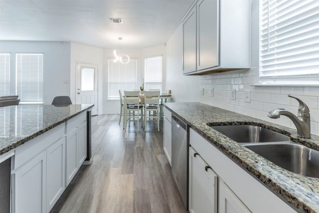 Kitchen with decorative backsplash, visible vents, light wood-type flooring, dishwasher, and a sink | Image 7