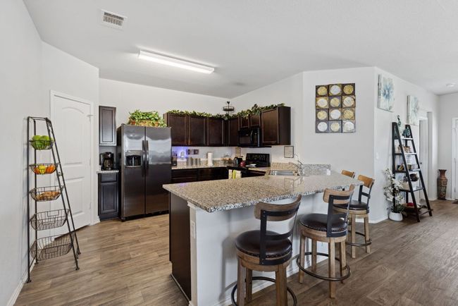 Kitchen with black appliances, wood-vinyl finished floors, dark brown cabinetry, light stone counters, and a peninsula | Image 5