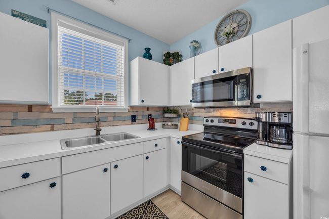 Kitchen featuring appliances with stainless steel finishes, a sink, white cabinetry, and light countertops | Image 9