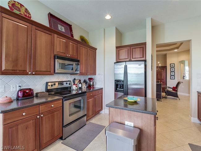 Kitchen featuring a center island, light tile flooring, backsplash, and appliances with stainless steel finishes | Image 8