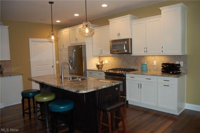 Kitchen featuring decorative light fixtures, dark hardwood / wood-style flooring, white cabinetry, and stainless steel appliances | Image 3