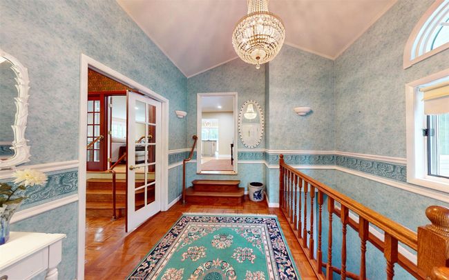 Hallway featuring wallpapered walls, french doors, lofted ceiling, plenty of natural light, and a chandelier | Image 22