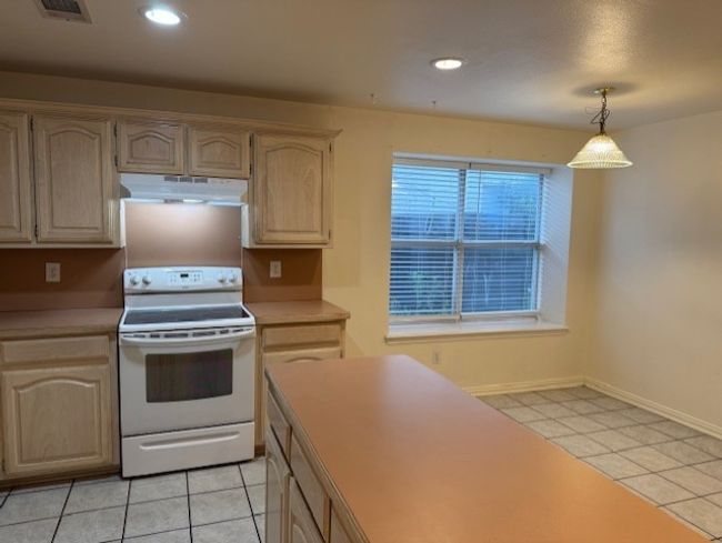 Kitchen with light tile patterned floors, electric stove, light countertops, under cabinet range hood, and recessed lighting | Image 8