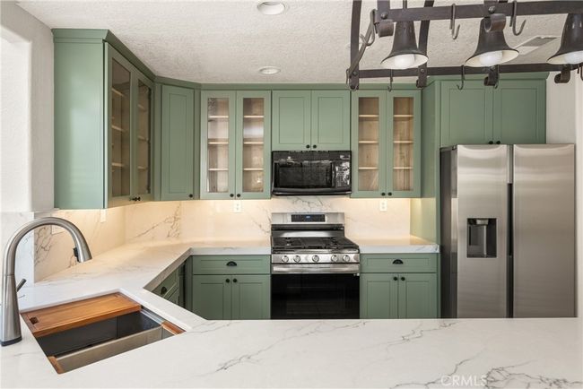 The open-concept kitchen features stainless steel appliances, a wine fridge, and flows seamlessly into the living area with a cozy fireplace and access to a private patio. | Image 14