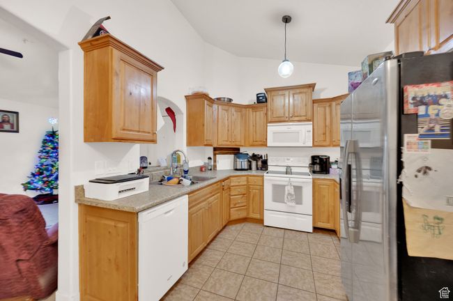 Kitchen featuring white appliances, vaulted ceiling, light countertops, light tile patterned floors, and pendant lighting | Image 4